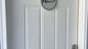 Eine weiße Tür mit einem runden Schild, auf dem 'Abbracci' steht, und einem Schlüsselloch.