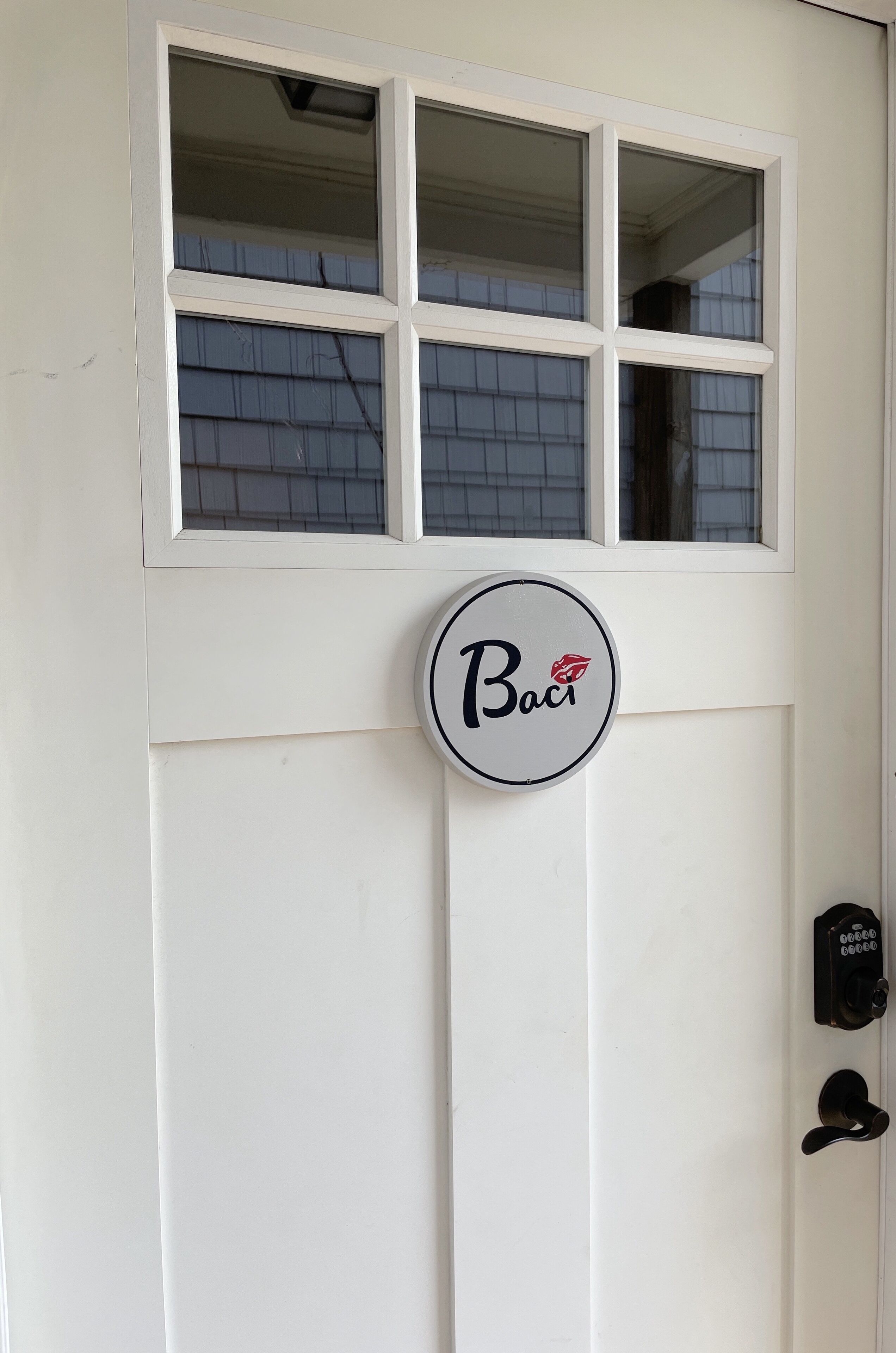 A white door with a window above it and a circular sign with the word "Baci" and a red lip design.