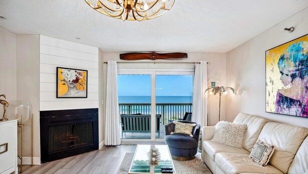 A living room with a fireplace, a sofa, a coffee table, and a view of the ocean through a sliding door. - Pelican Pointe 5B (Indian Shores)
