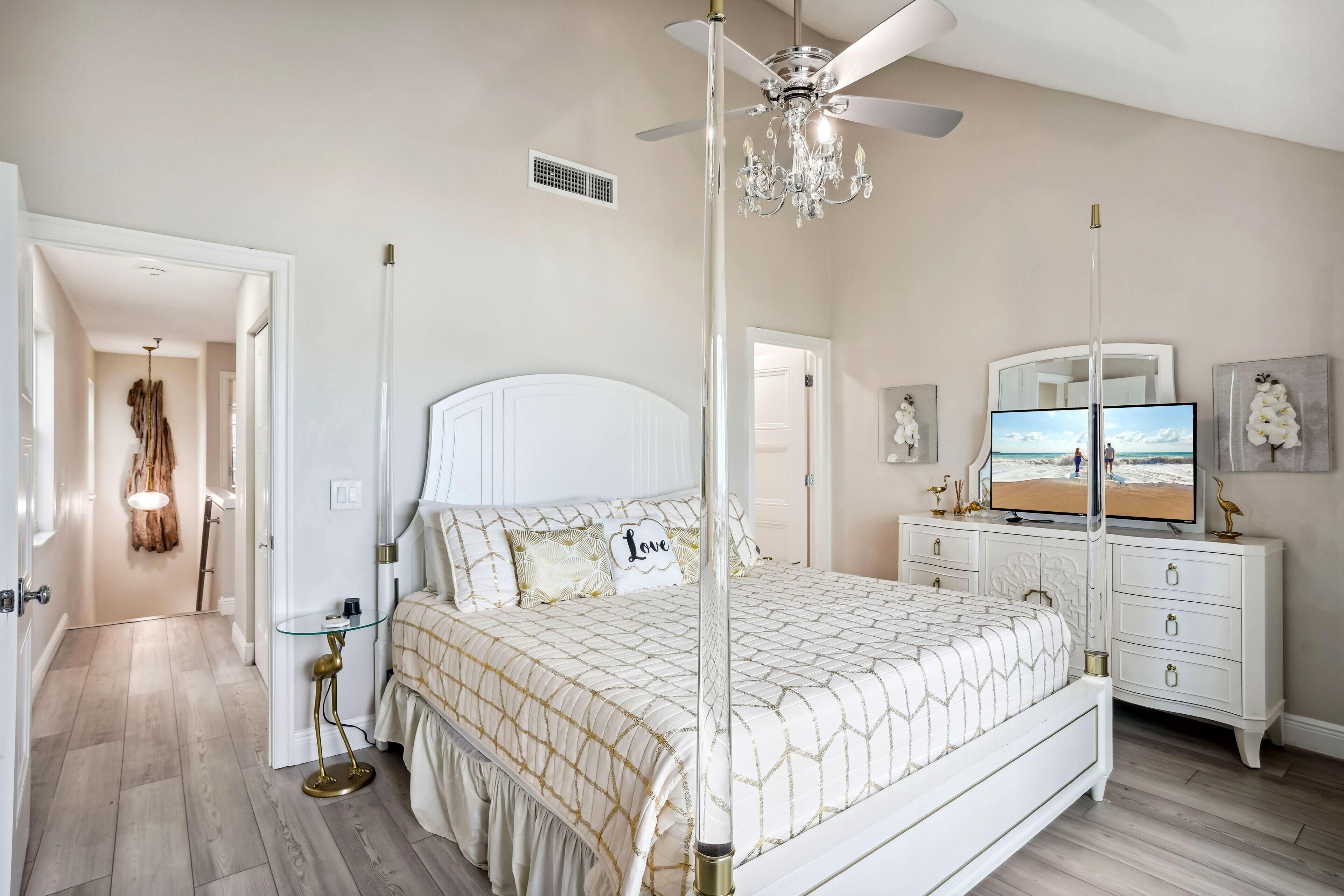 A bedroom with a bed, bedside tables, a dresser, a ceiling fan, a chandelier, and a television.