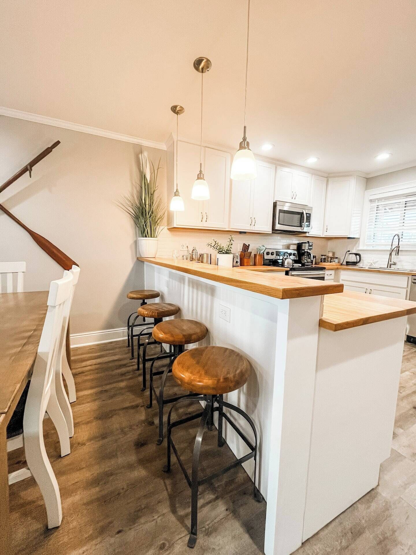 A modern kitchen with white cabinets, a wooden countertop, and three bar stools.