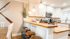 A modern kitchen with white cabinets, a wooden countertop, and three bar stools. - Oceanview condo in heart of PSJ Beach (Port St. Joe)