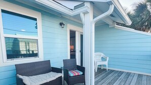 A covered outdoor seating area with wicker furniture and a table, a door leading to an interior space, and a light blue exterior wall. - Oceanview condo in heart of PSJ Beach (Port St. Joe)