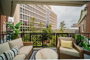 Un balcon agrémenté de meubles en osier, d’une table ronde et offrant une vue sur un immeuble moderne.
