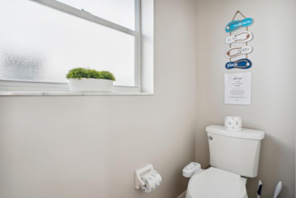 A bathroom with a toilet, a hand dryer, a paper towel dispenser, a small potted plant, and a window with a view. - Mariner's Pointe 701 (Indian Shores)