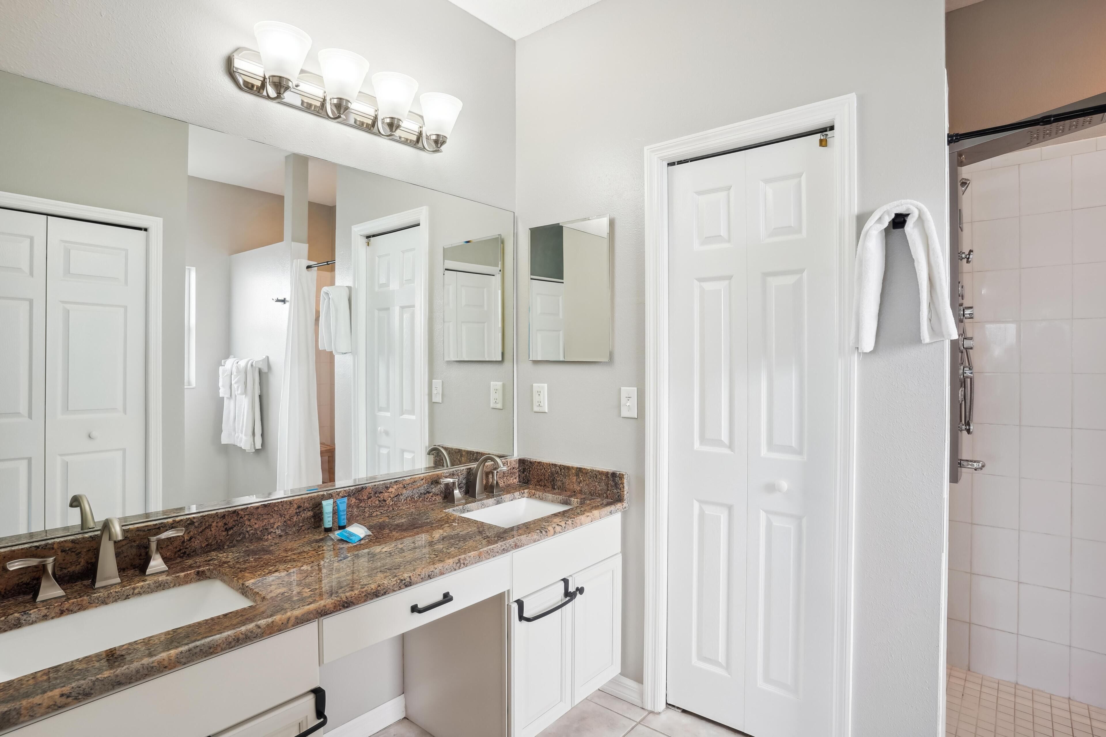 A bathroom with a granite countertop sink, a large mirror, and a white shower.