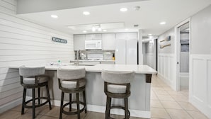A modern kitchen with a bar area, white cabinetry, and a sign reading "BEACH HOUSE". - Holiday Villas II 407 Premier (Indian Shores)
