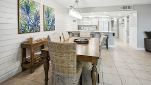 A modern dining area with a long wooden table, wicker chairs, and two abstract paintings on the wall. - Holiday Villas II 407 Premier (Indian Shores)