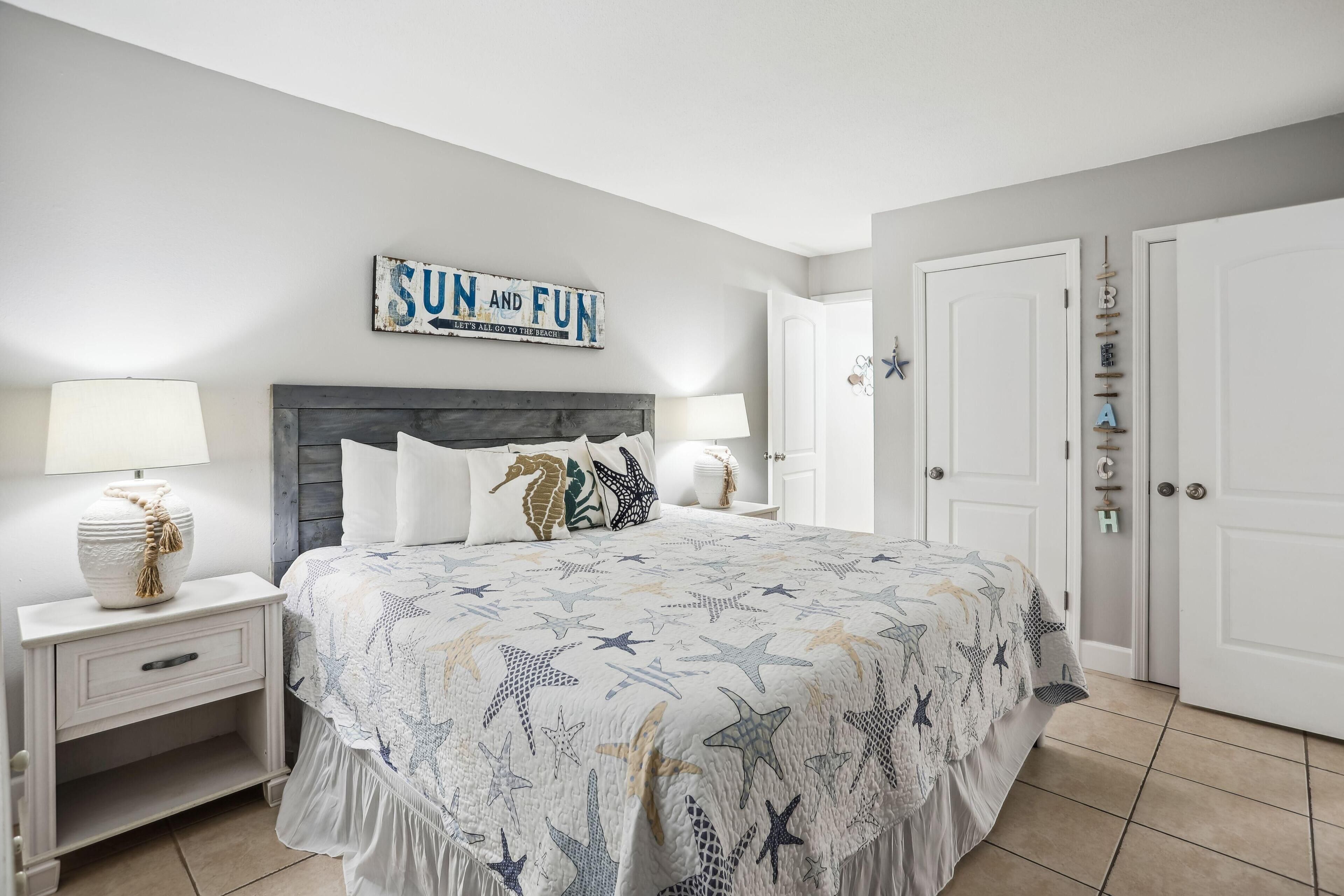 A bedroom with a bed, nightstands, a wall sign, and a door.