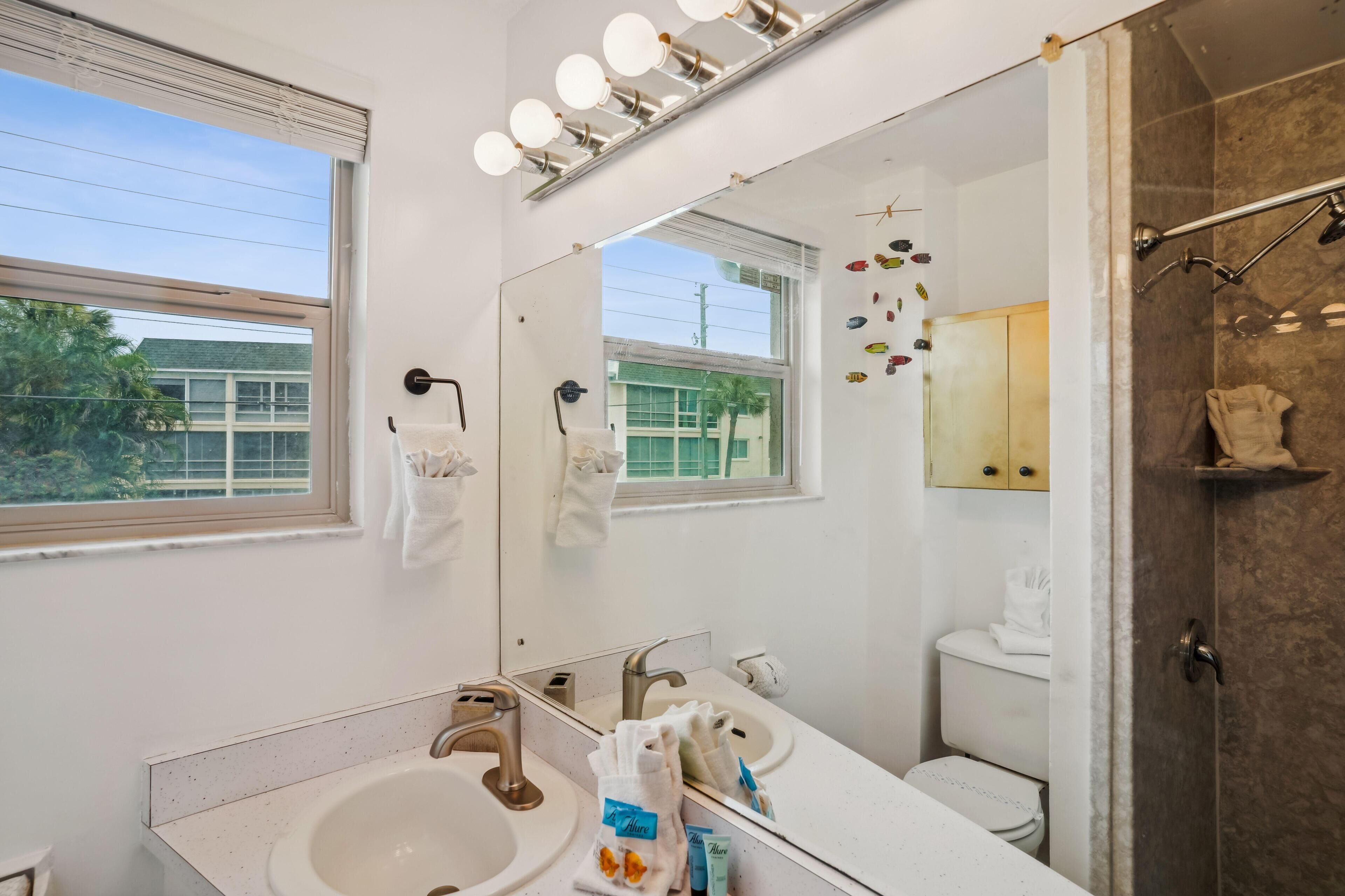 Een badkamer met een grote spiegel, twee wastafels, een douche en een raam.