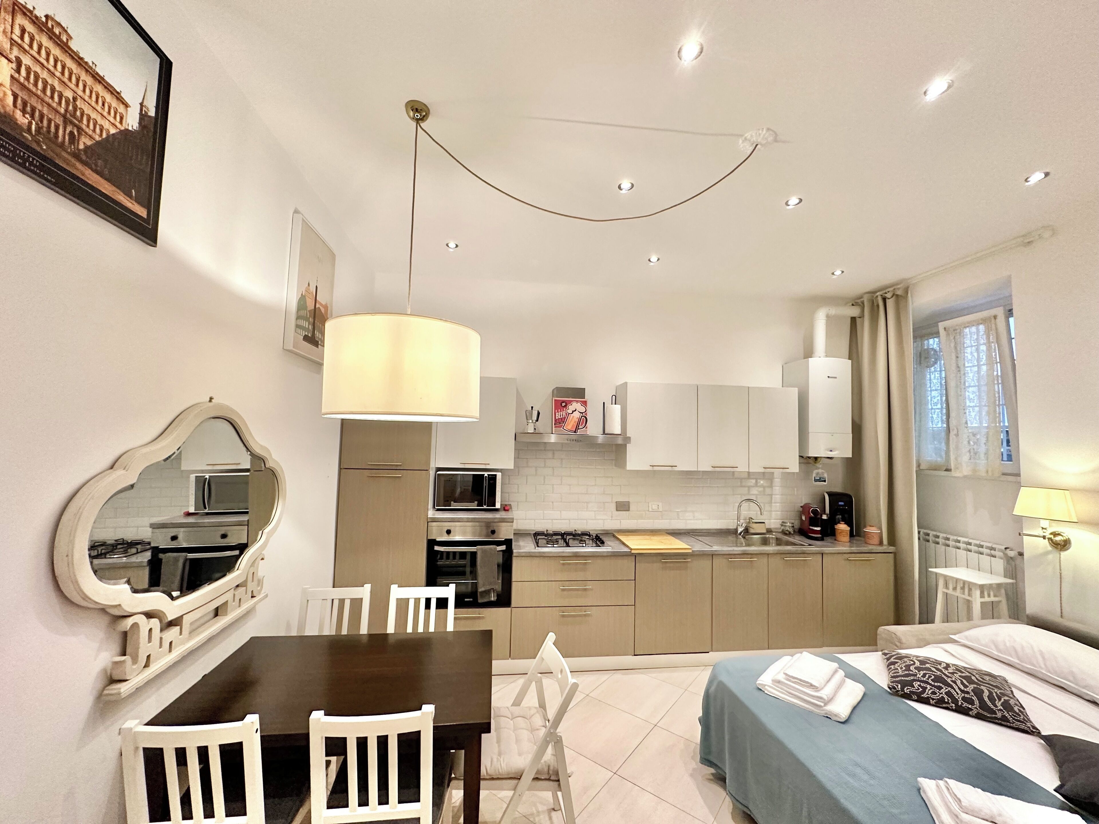 A compact hotel room with a dining area, kitchenette, and a bed with a blue bedspread.