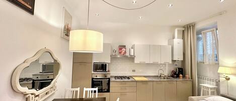 A compact hotel room with a dining area, kitchenette, and a bed with a blue bedspread.