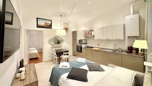 Ett modernt hotellrum med en säng, ett nattduksbord, ett skrivbord, en stol och ett litet kök.
