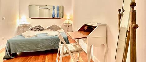 A modern bedroom with a bed, bedside tables, a desk, a mirror, and a hanging light fixture.
