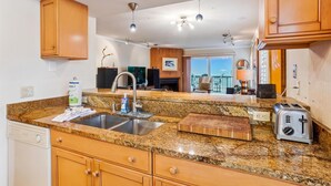A kitchen with granite countertops, wooden cabinets, a stainless steel sink, a toaster, and a ceiling fan. - Pelican Pointe 3B (Indian Shores)