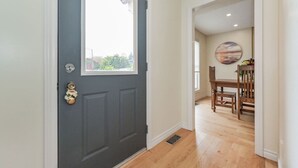 A hallway with a dark gray door, a window, and a dining area with a wooden table and chairs. - (A)  Elora Grand River Suite (Elora)