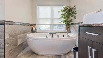 Een moderne badkamer met een vrijstaand bad, een raam en een potplant.