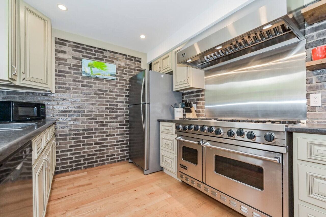 A modern kitchen with a brick wall backsplash, stainless steel appliances, and light-colored cabinetry.