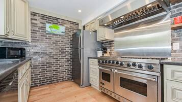 A modern kitchen with a brick wall backsplash, stainless steel appliances, and light-colored cabinetry.