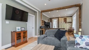 A living room with a grey sofa, a wooden cabinet, and a TV on the wall. - (C) Elora Riverview Flat (Elora)