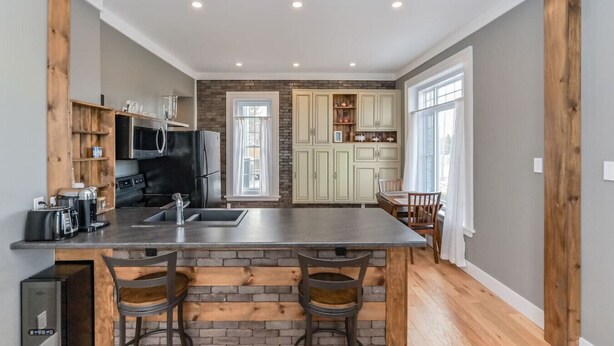 A modern kitchen with a central island, built-in appliances, and a dining area with a table and chairs. - (C) Elora Riverview Flat (Elora)