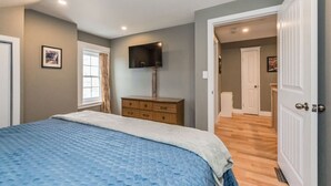 A bedroom with a bed, a dresser, a TV mounted on the wall, and a door leading to another room. - (C) Elora Riverview Flat (Elora)