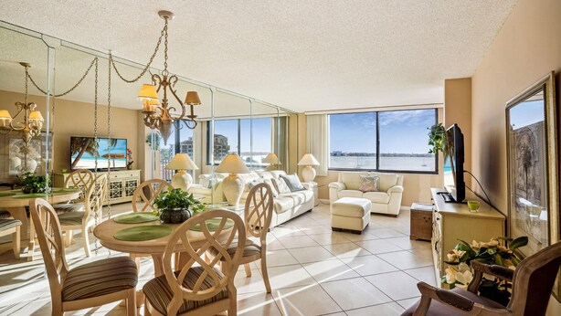 Amplia sala de estar con mesa de comedor, sillas, sofás y un gran ventanal con vista al mar.