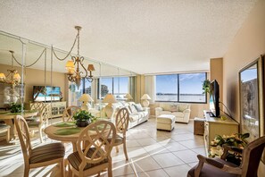 Amplia sala de estar con mesa de comedor, sillas, sofás y un gran ventanal con vista al mar.