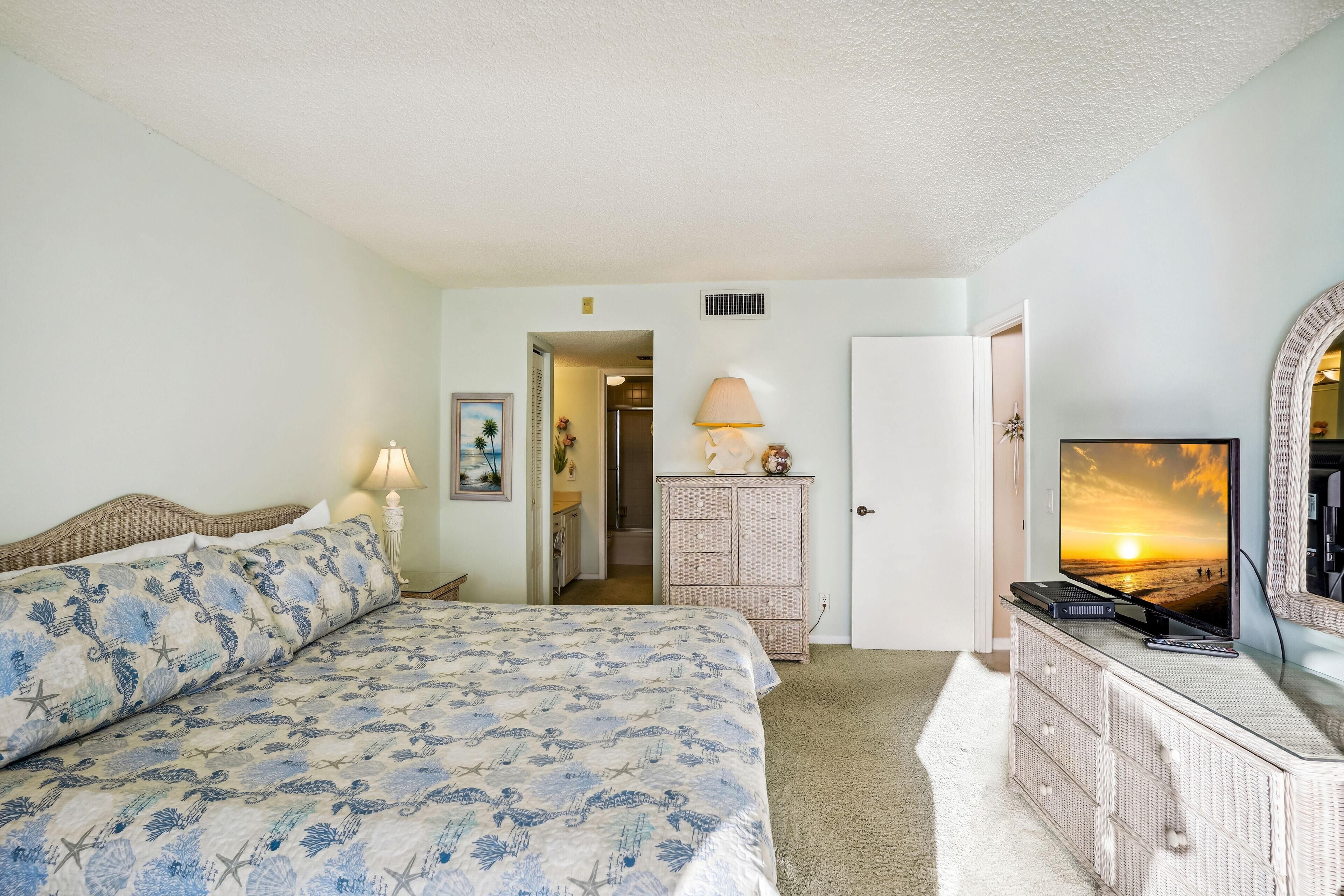 Un dormitorio con una cama, televisión, lámpara y una puerta que da a otra habitación.