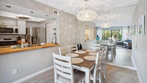 A modern kitchen with a wooden countertop, white cabinetry, and a dining area with a wooden table and chairs. - Land's End 1-306 Bay Front- Premier (Treasure Island)