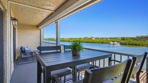A balcony with a table and chairs, overlooking a body of water with boats and greenery. - Bayshore Yacht & Tennis 409 - Premier (Indian Shores)