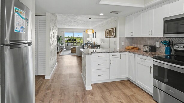 A modern kitchen with white cabinetry, stainless steel appliances, and a herringbone-patterned backsplash. - Bayshore Yacht & Tennis 409 - Premier (Indian Shores)