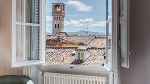 A bedroom with a large window overlooking a historic tower and tiled rooftops. - Modern Panoramic Penthouse with Elevator inside the Walls of Lucca (Lucca)