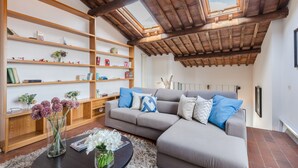A living room with a grey sectional sofa, wooden bookshelves, and a round coffee table with flowers. - Modern Panoramic Penthouse with Elevator inside the Walls of Lucca (Lucca)