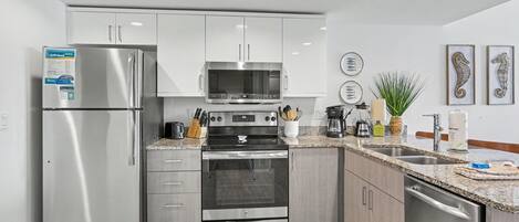 A modern kitchen with stainless steel appliances, granite countertops, and white cabinetry.