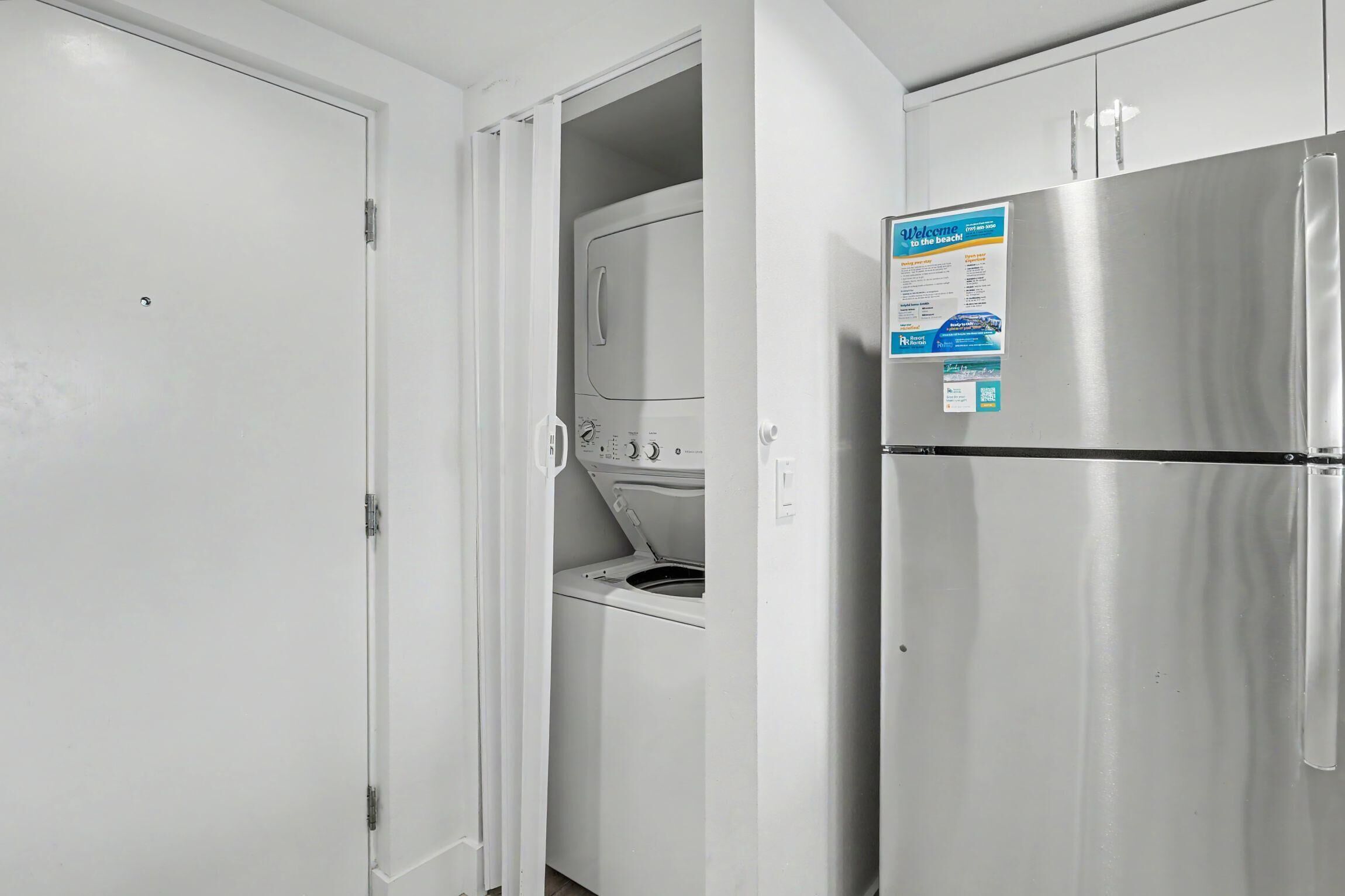 Een keuken met een roestvrijstalen koelkast, een wasmachine en een deur met een bordje.