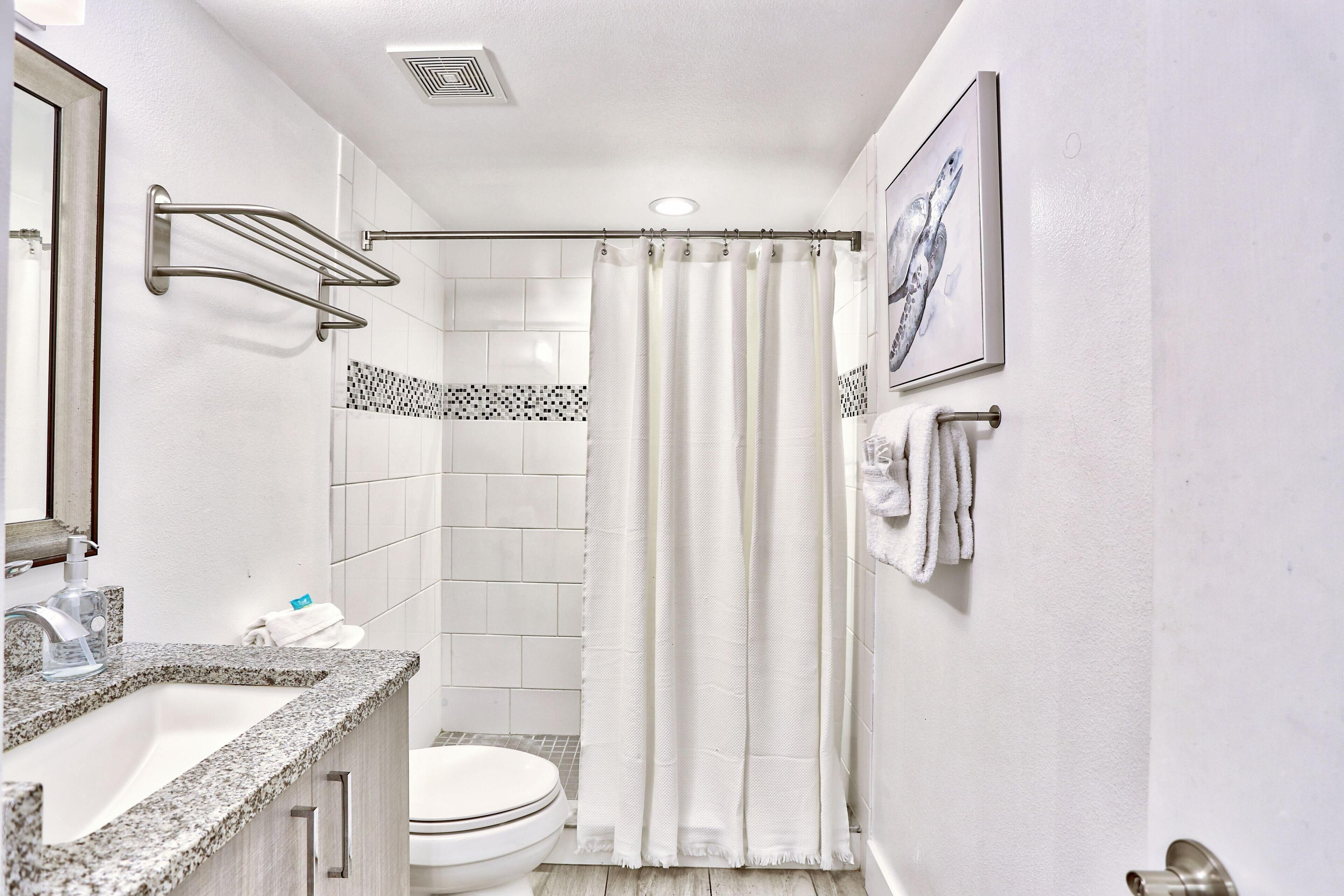 A bathroom with a shower curtain, a toilet, a sink with a mirror, and a towel rack.