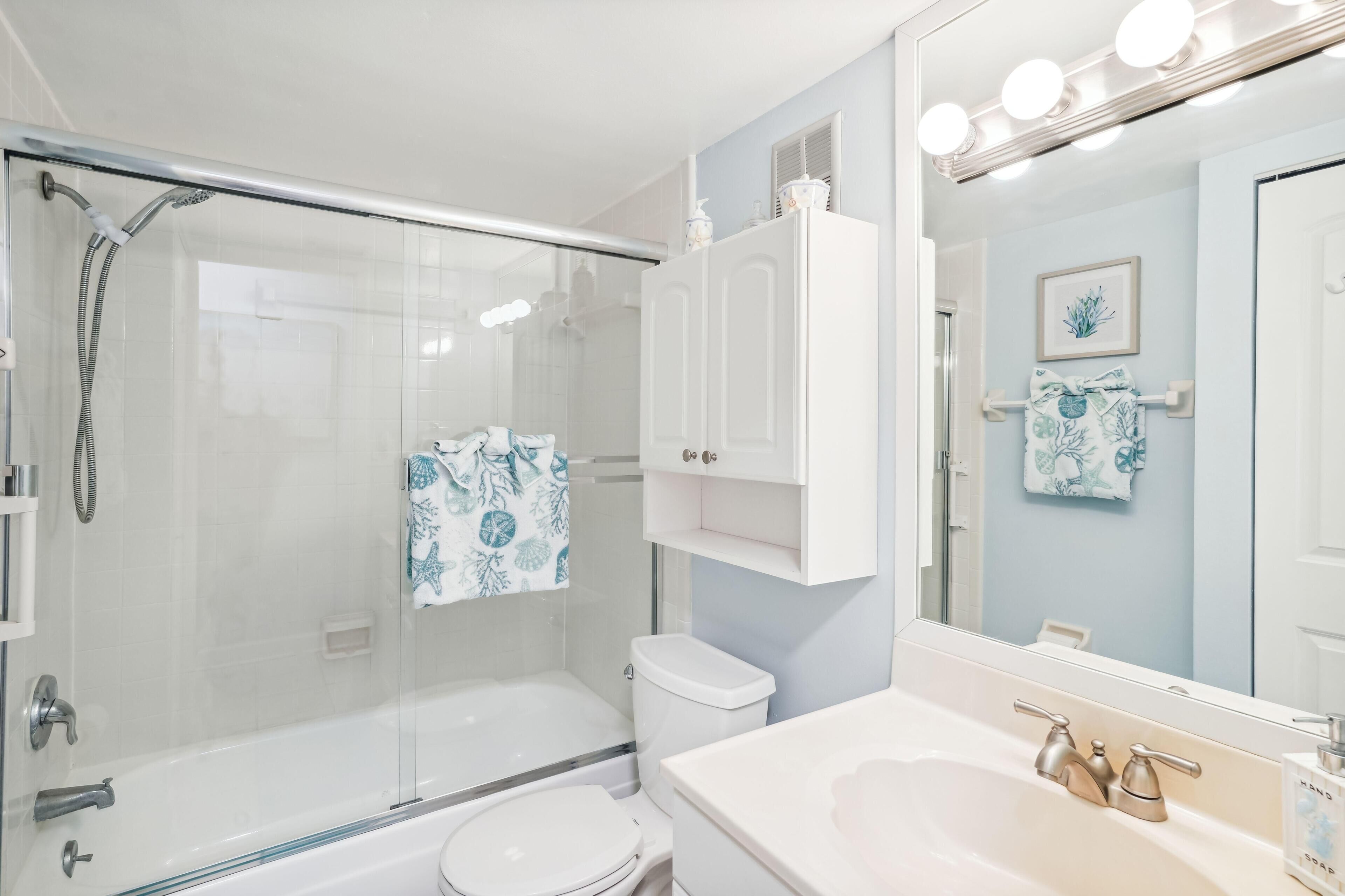 Een moderne badkamer met een douchecabine van glas, een wit toilet, een wastafel met een wastafel en spiegel, en een wandgemonteerde apothekerskast.