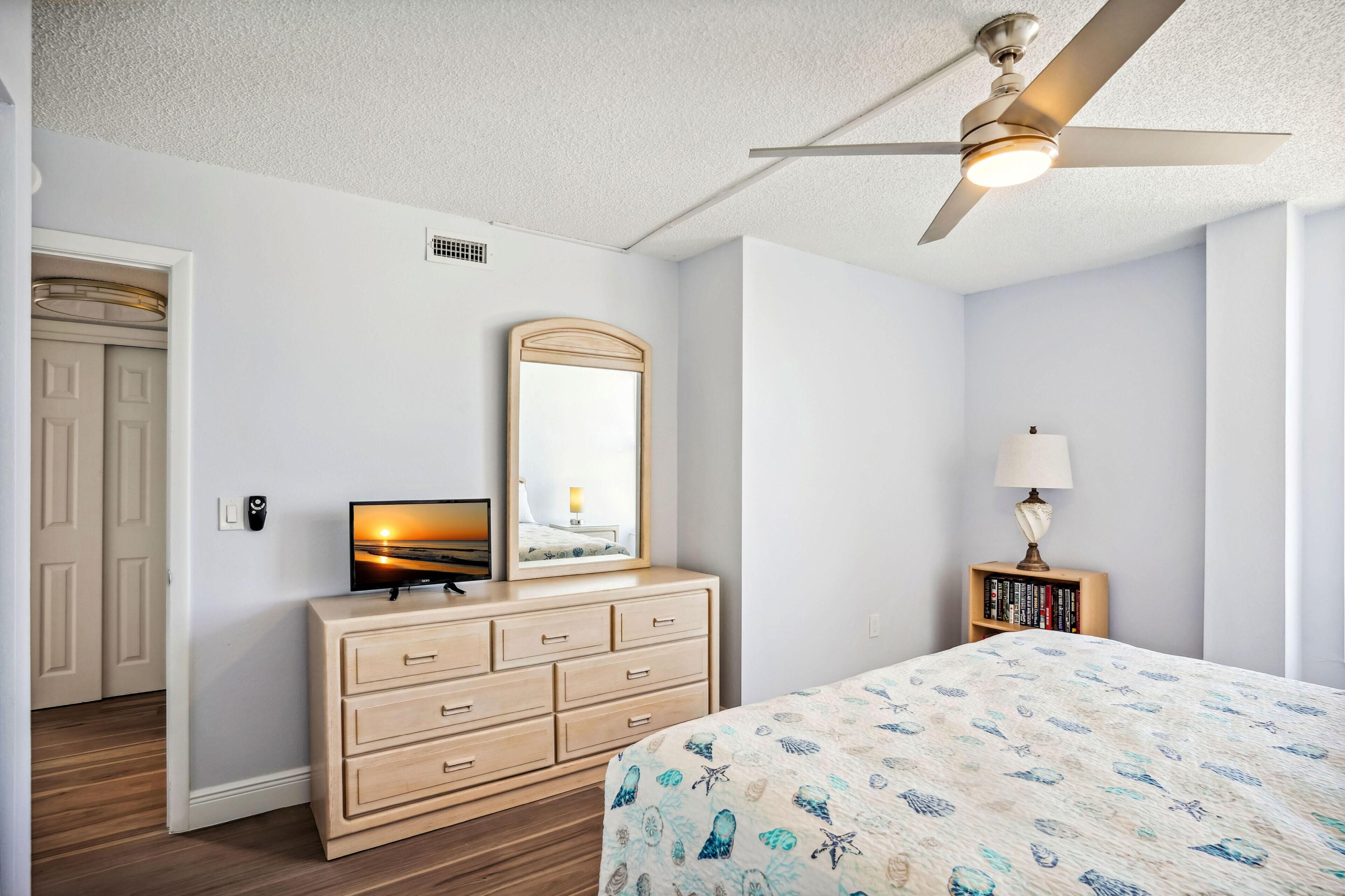 Un dormitorio con cama, cómoda, televisor y ventilador de techo.
