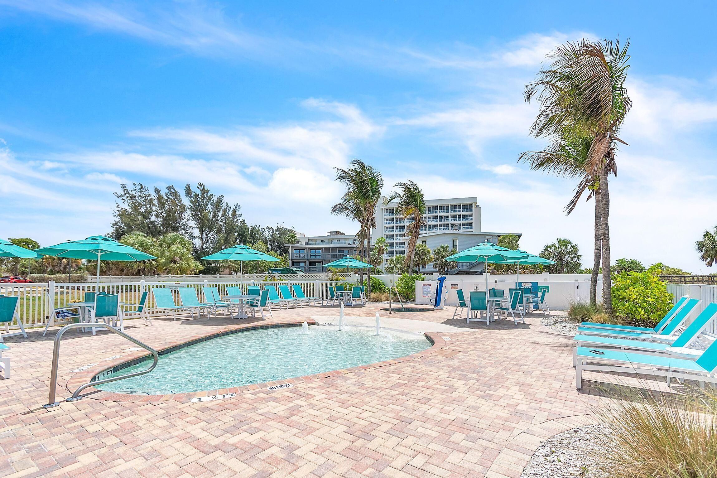 A pool area with lounge chairs and umbrellas, a pool, and a building in the background.