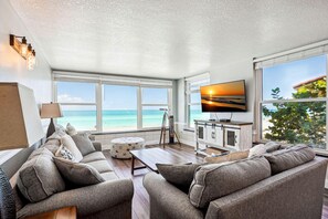 Ein Wohnzimmer mit großem Fenster zum Meer, einem Flachbildfernseher und einer gemütlichen Sitzecke.