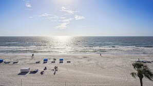 Ein Strand mit sonnendurchflutetem Sand, ein paar Personen und eine Palme.