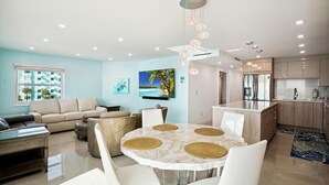 Ein modernes Wohnzimmer mit einem runden Esstisch, beigefarbenen Sofas und einer Küchenzeile mit Holzschränken und Edelstahlgeräten.