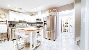 A modern kitchen with white cabinets, stainless steel appliances, and a wooden island with bar stools.