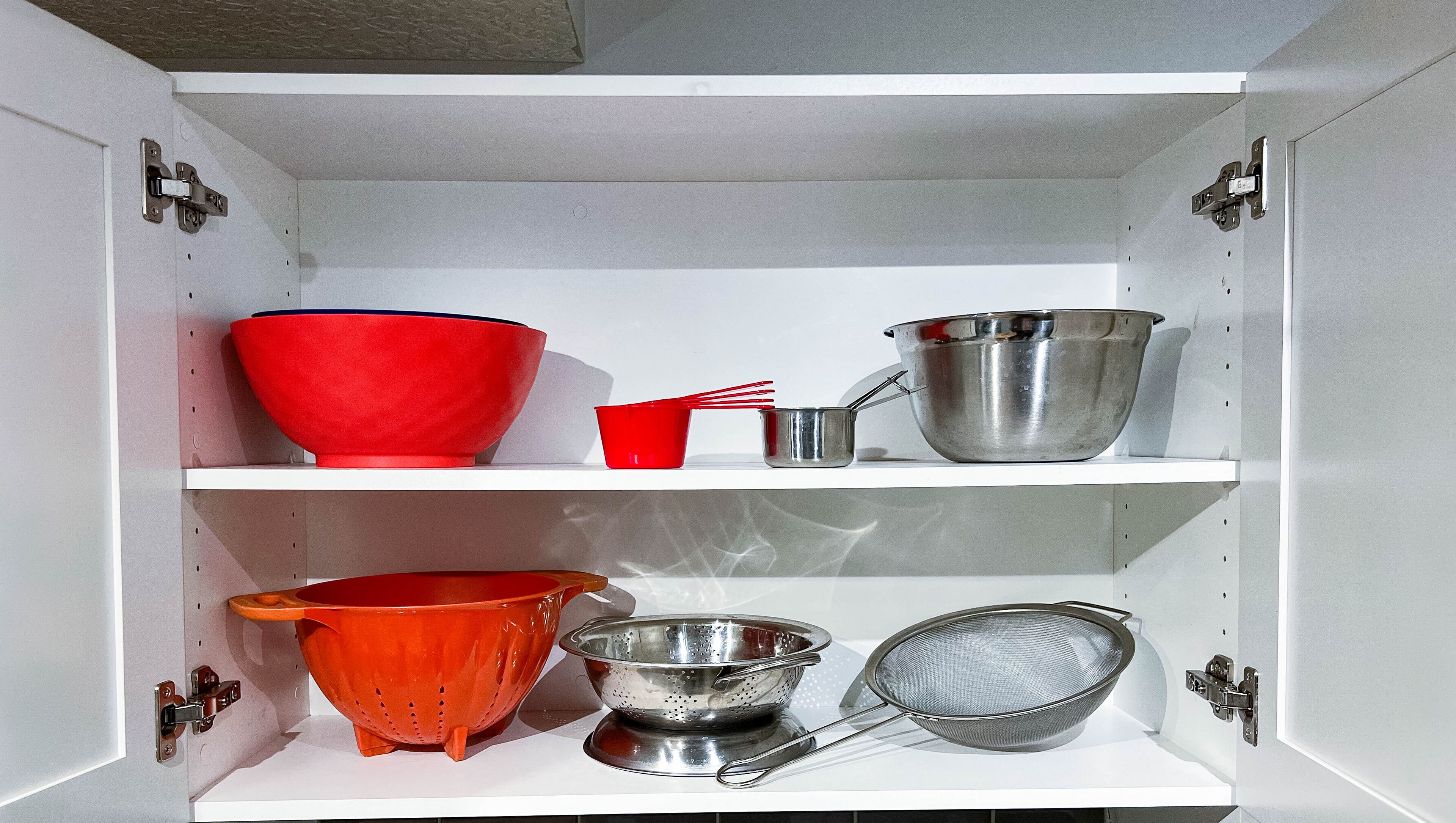 A kitchen cabinet with shelves holding various kitchen utensils and cookware.