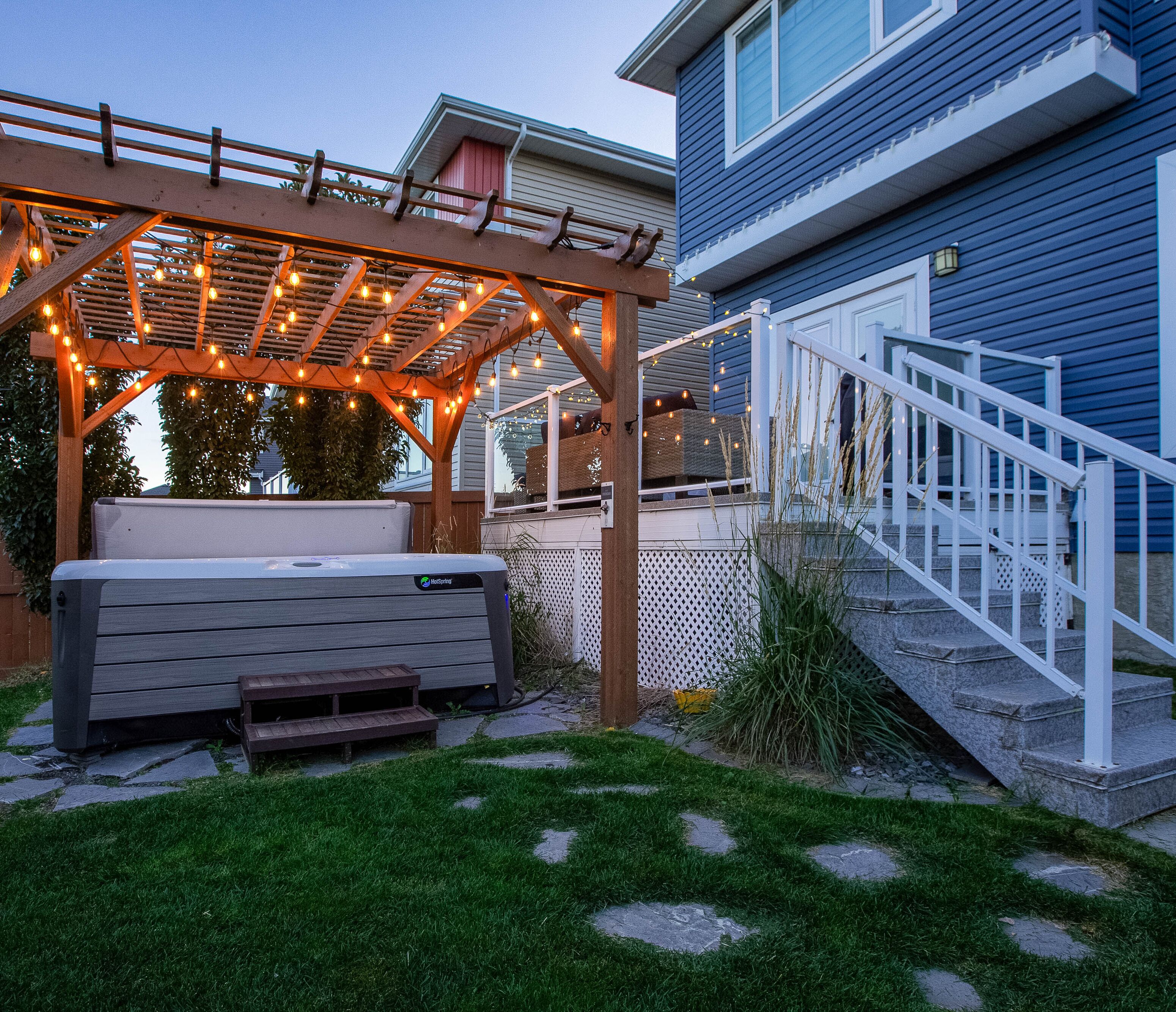 Un área de estar exterior techada con luces colgantes, un banco y una escalera que lleva a una casa.