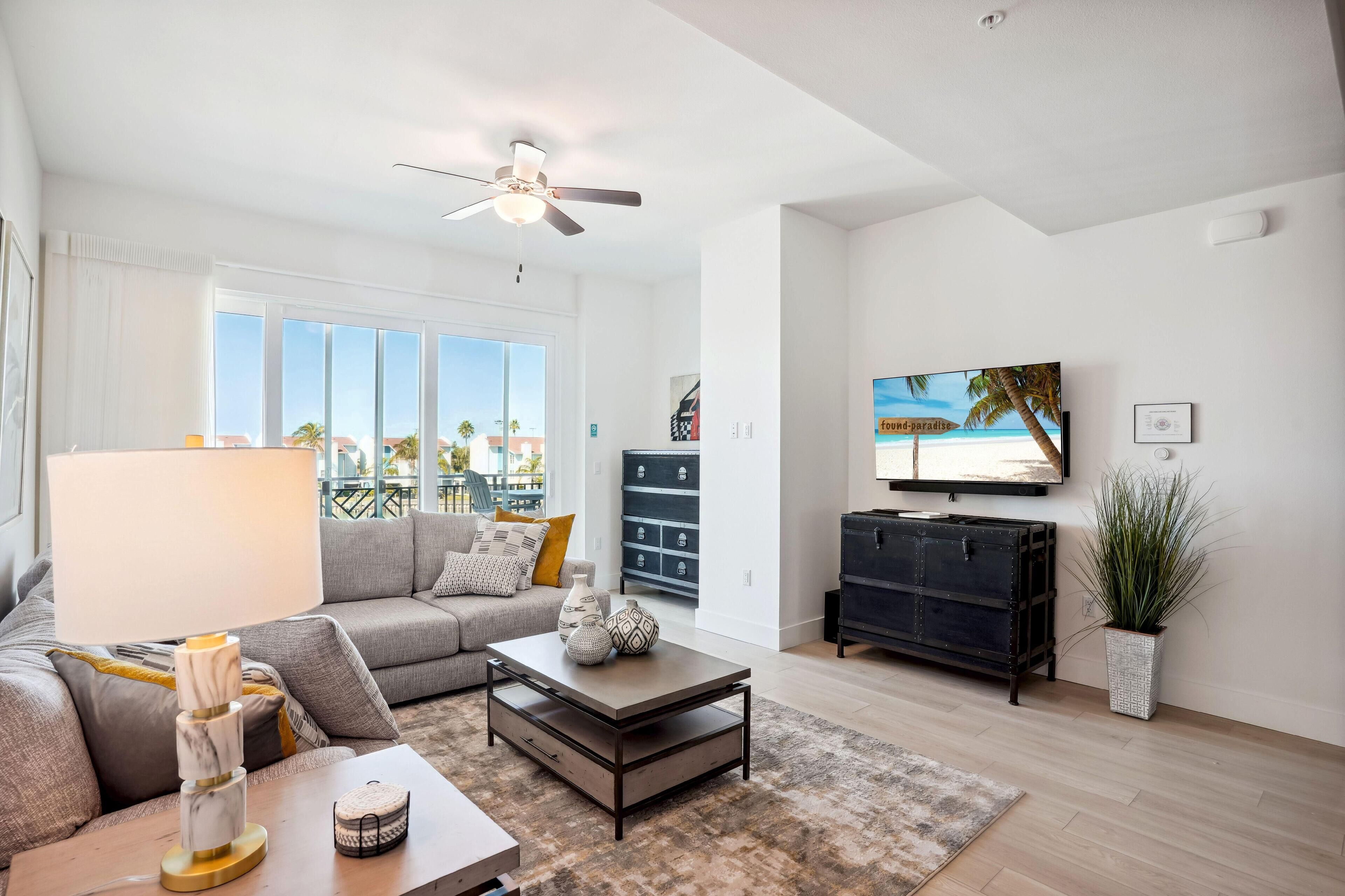 A modern living room with a grey sofa, a coffee table, a TV, and a ceiling fan.