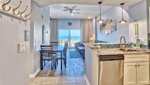 A modern kitchen with a dishwasher, a dining area with a table and chairs, and a view of the ocean through large windows. - Madeira Bay Resort I 1502 (Madeira Beach)