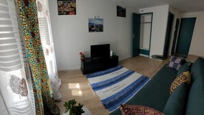 A living room with a sofa, a TV, a striped rug, and a small table with a plant. - Maison Pour Vacances (Marseille)