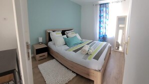A bedroom with a wooden bed, a nightstand, a white rug, and a window with curtains. - Maison Pour Vacances (Marseille)